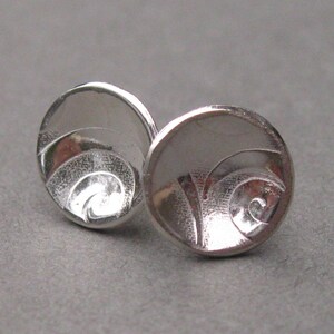 May include: A pair of silver earrings featuring a swirling design. The earrings are round and have a smooth, polished finish.