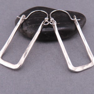 Könnte beinhalten: Ein Paar silberne, gehämmerte rechteckige Creolen. Die Ohrringe sind aus Sterlingsilber und haben eine gehämmerte Oberfläche.