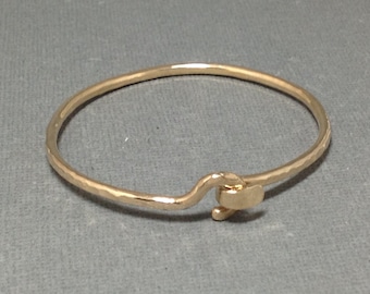 May include: A gold hammered bangle bracelet with a simple hook closure.