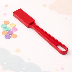 Könnte beinhalten: Ein roter Magnetstab mit Griff und rechteckigem Kopf, neben einer Sammlung bunter, runder Magnetchips. Der Stab hat ein Loch am Ende des Griffs. Die Chips sind in verschiedenen Farben.