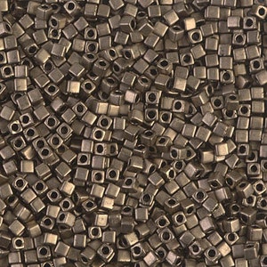 May include: Close-up of a pile of small, square, metallic beads. Each bead has a hole in the centre. The beads are a muted, bronze colour and are scattered randomly, creating a textured surface.