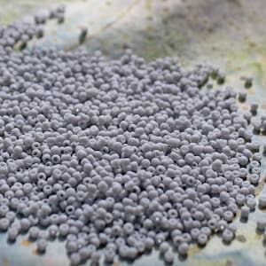 May include: A large pile of small, light gray seed beads. The beads are round and have a smooth, shiny finish.