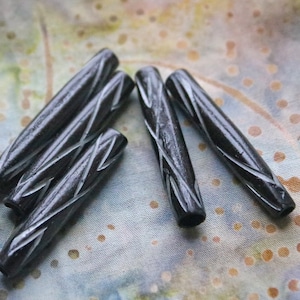 May include: Five black wooden beads with a carved design. The beads are cylindrical and have a smooth, polished finish.