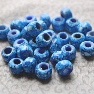 May include: A collection of blue and white marbled glass beads. The beads are round and have a hole in the centre. They are perfect for making jewellery or other crafts.