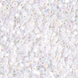 May include: A close-up of a pile of white iridescent square seed beads. The beads are small and have a subtle shimmer.