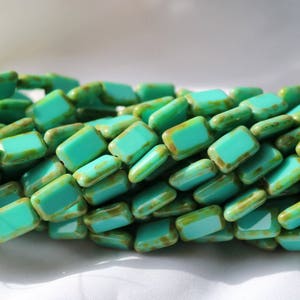 May include: A strand of turquoise blue glass beads with a green and brown mottled finish. The beads are rectangular in shape and have a slightly irregular edge.