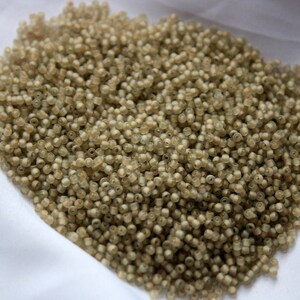 May include: A large pile of small, light brown seed beads. The beads are round and have a slightly translucent appearance.