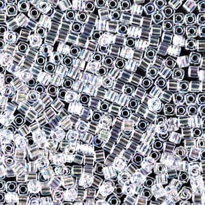 May include: A close-up view of a large quantity of small, clear, iridescent square beads. The beads have a hole in the center and are arranged in a random pattern.