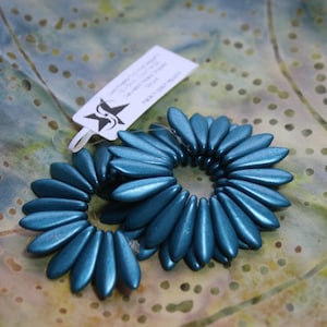 May include: Two teal blue flower-shaped bead strands made of small, elongated beads. The beads are arranged in a circular pattern, creating a flower-like design.