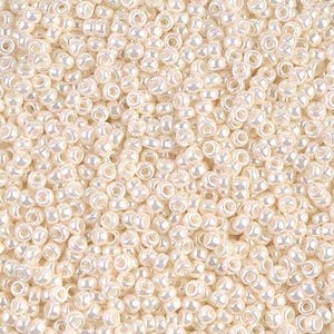 May include: A close-up shot of a pile of small, off-white seed beads. The beads are uniform in size and shape, with a pearlescent sheen. They are densely packed together, filling the frame.