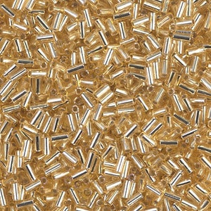 May include: A close-up image of a large quantity of gold-colored glass beads. The beads are small and cylindrical in shape.