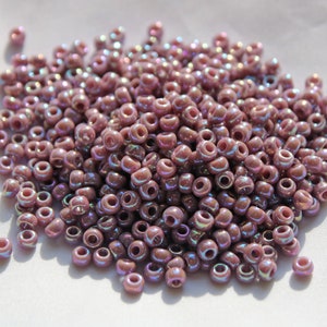May include: A large pile of iridescent purple seed beads. The beads are small and round, and they have a slight shimmer to them.