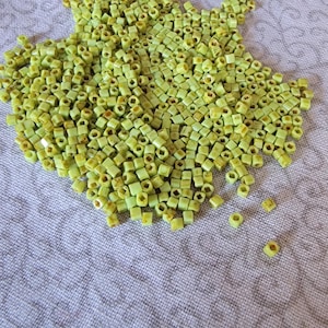 May include: A large pile of light green square beads. The beads are made of glass and have a slightly iridescent finish.