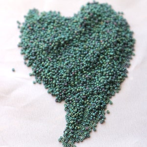 May include: A heart-shaped pile of small, iridescent green beads on a white surface.