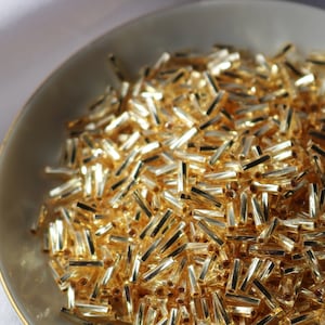 May include: A bowl filled with gold-colored glass beads. The beads are small and cylindrical in shape.