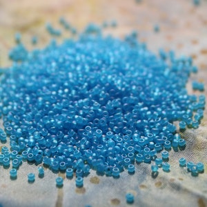 May include: A large pile of small, light blue glass beads on a textured fabric surface.