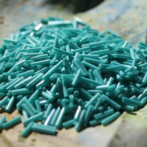 May include: A large pile of turquoise blue glass beads, each bead is a long cylinder shape.