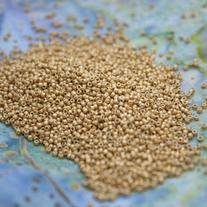 May include: A large pile of small, round, gold-colored beads. The beads are scattered on a blue and white patterned surface.