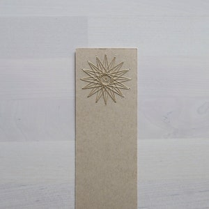 May include: A brown cardboard bookmark with a gold star design in the center.