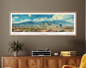May include: A framed panoramic art print of Colorado Springs, featuring a cityscape with mountains in the background. The artwork has a light wood frame and includes the text "Colorado Springs" and "Little London". The coordinates 38.87°N 104.76°W are also visible.