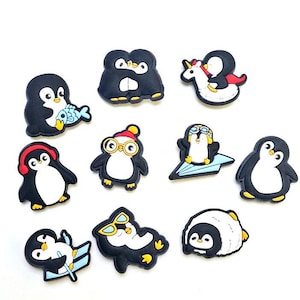 May include: A selection of black and white penguin charms, each with a unique design. Some penguins are depicted with accessories like fish, headphones, and glasses. One penguin rides a unicorn. These charms are likely for shoes or other accessories.