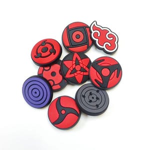May include: A selection of colourful, circular charms with various designs. The charms feature red, black, grey, and purple colours. Some designs include swirling patterns, geometric shapes, and a red cloud. These charms are likely for decorative purposes.
