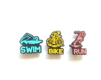 May include: Three black and yellow shoe charms with the words "Swim", "Bike", and "Run" on them. The charms feature a swimmer, a cyclist, and a runner.