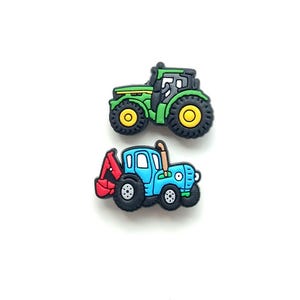 May include: Two rubber shoe charms shaped like tractors. The top charm is a green tractor with yellow wheels and black detailing. The bottom charm is a blue tractor with black wheels, a red backhoe attachment, and a brown exhaust pipe on the side.