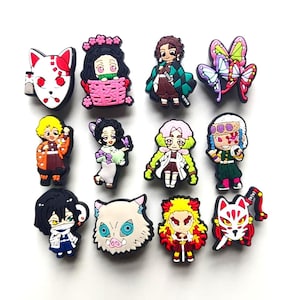 May include: A set of eleven colourful rubber shoe charms featuring various anime-inspired characters, including a white fox mask, a character in a pink basket, a butterfly motif, and several figures with distinct hair colours and outfits in a grid.