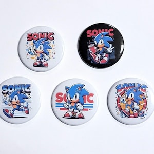 May include: Five round Sonic the Hedgehog buttons. Each button features a different image of Sonic, including a running Sonic, a Sonic holding a drink, and a Sonic with a thumbs up. The buttons are all white with red and blue accents.
