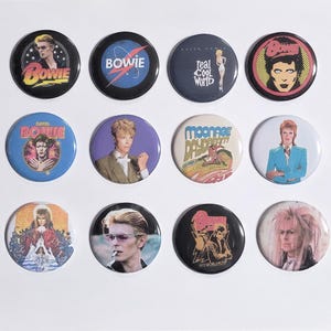 May include: A collection of twelve circular pin-back buttons featuring various graphic designs and photographic portraits of David Bowie. The buttons display diverse imagery including album art, concert tour graphics, and iconic film character stills.