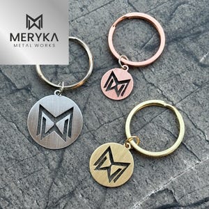 May include: Three keychains with different colored metal rings and a circular charm with a cut-out M logo. The charms are silver, gold, and rose gold.