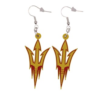 May include: A pair of gold-colored earrings with a trident design. The trident is outlined in red and has a silver hook. The earrings are a dangle style and are set against a white background.