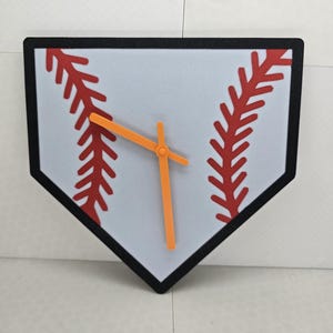 May include: A white baseball home plate shaped clock with red stitching and orange hands.