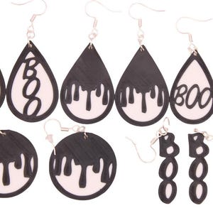 May include: A collection of Halloween-themed earrings. The earrings feature black and white designs, including teardrop shapes with the word "BOO", dripping paint effects, and circular shapes. The earrings are suspended from silver-colored hooks.