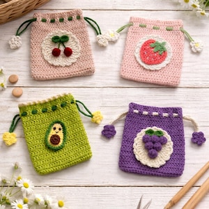 Peut inclure: Quatre pochettes à cordon crochetées à la main en rose, vert et violet, chacune avec un motif de fruit différent : cerises, fraise, avocat et raisins. Les pochettes ont un fond circulaire blanc et sont sur une surface en bois blanc.
