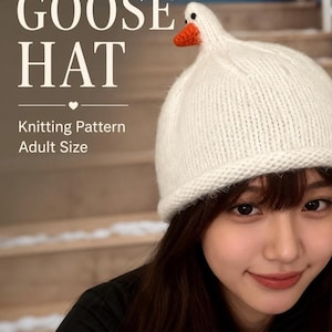 May include: A white knitted goose hat with an orange beak. The hat is adult size and features the text "GOOSE HAT" and "Knitting Pattern". The hat is worn by a person.