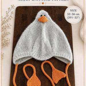 May include: A grey knitted goose hat with an orange beak, black eyes, and orange dangling ties with triangular ends. The text reads GOOSE HAT ADULT KNITTING PATTERN, SIZE 52-56 cm (20.5-22 inches), and Design by Ellen Ganzburg aka ElleGanT.