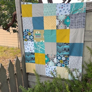 May include: A patchwork quilt with a variety of patterns and colors, including yellow, blue, green, and white. The quilt is made up of squares and rectangles, and some of the squares have a typewriter design.