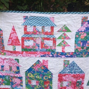 May include: A colorful quilt with a patchwork design featuring houses, trees, and the text "Hotel Fredericksburg". The quilt is made with a variety of floral fabrics in shades of pink, blue, green, and white.