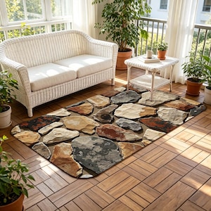 Puede incluir: Una alfombra rectangular con un diseño de piedra en tonos grises, marrones y beige. La alfombra está colocada sobre un suelo de madera, con un sofá y una mesa auxiliar de mimbre blanco en el fondo. Las plantas en macetas añaden un toque de vegetación.