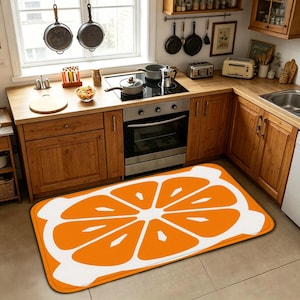 Peut inclure: Un tapis de sol de cuisine rectangulaire présentant un grand motif stylisé de tranche d'orange. Le design se compose de segments orange vifs disposés en cercle sur un fond blanc, avec une bordure blanche texturée entourant le fruit.