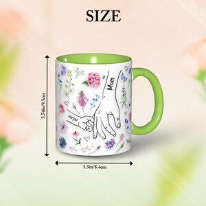 May include: White ceramic mug with a green interior and handle. The mug features a floral design with the words "Mom" and "Harper" on a hand-holding illustration. The mug is 3.74 inches (9.5cm) tall and 3.3 inches (8.4cm) wide.