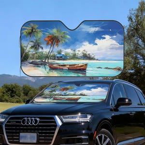 May include: Black car with a windshield sunshade featuring a tropical beach scene. The sunshade displays a painting of a boat on the water, palm trees, and a blue sky with clouds. The car is parked outdoors.