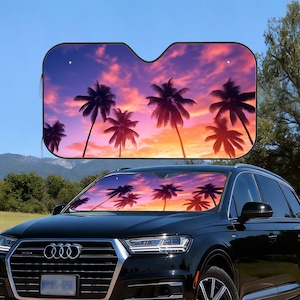 以下が含まれることがあります： ヤシの木のある夕焼けの風景が描かれた、フロントガラス用のサンシェードが付いた黒い車。サンシェードは黒い縁取りがあり、車のフロントガラスに取り付けられています。空はオレンジ、ピンク、紫色の混合色です。