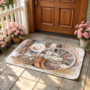 May include: Rectangular doormat with a rustic country theme. Features a wagon wheel, cowboy boots, a straw hat, and daisies. The background has a wooden plank design with blue accents. The mat is placed in front of a wooden door.