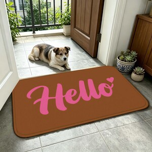 May include: A brown rectangular doormat with the word "Hello" in pink script and a small heart. A dog is lying down near the mat. The mat is placed in front of a door.