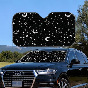 May include: Black car sunshade with a celestial pattern of white moons, stars, and dots. The sunshade is installed in the windshield of a black SUV, providing shade from the sun.
