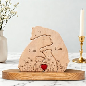 May include: A wooden bear family puzzle with the names "Brian", "Mom", "Emma", and "Ava" engraved on it. The puzzle features a red heart and floral details. It is displayed on a wooden base.