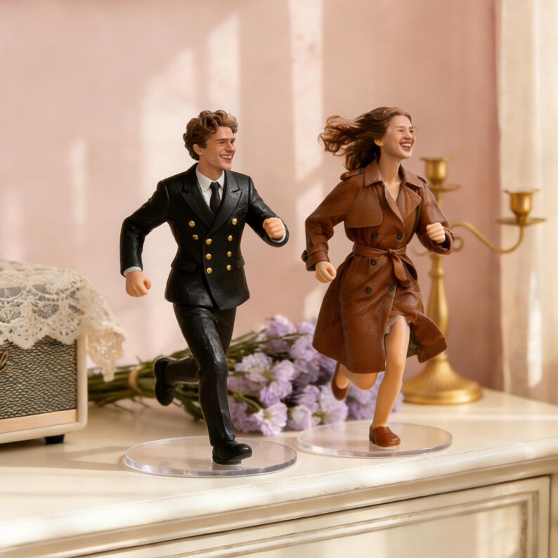 May include: Two figurines of a running couple. The man is wearing a black suit with gold buttons and a black tie. The woman is wearing a brown trench coat. Both figurines are on clear circular bases.